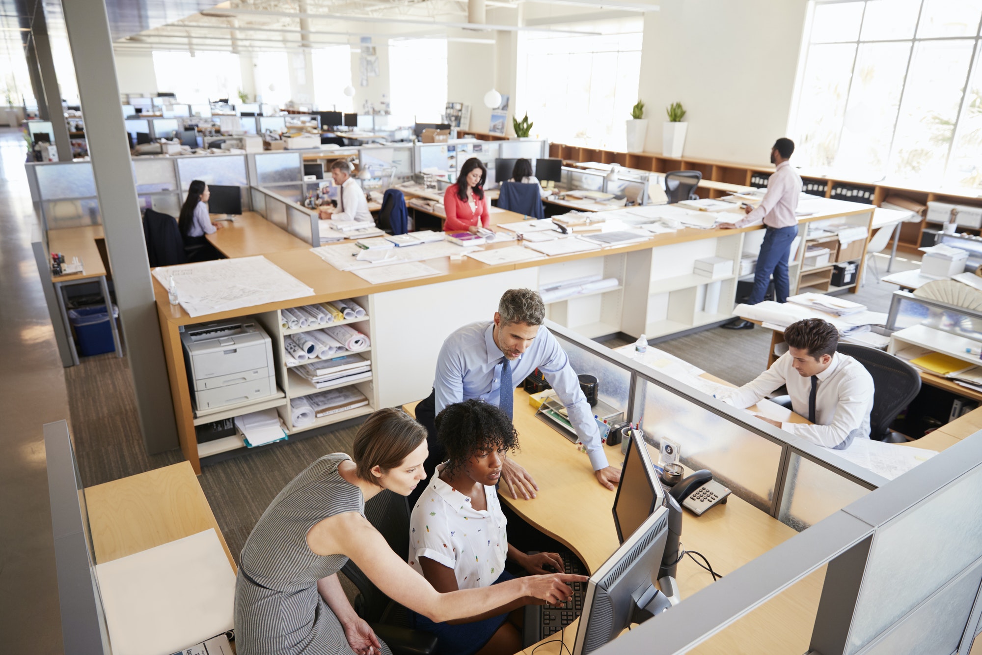 Colleagues working at a woman’s workstation in a busy office